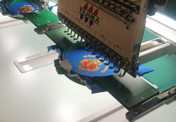 Multi-head embroidery machine stitching a crest onto a garment