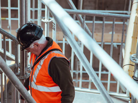 Construction worker in an orange hi-vis vest and hard hat among scaffolding