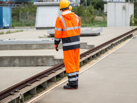 Worker in an orange high-visibility suit and hard hat standing beside a rail track