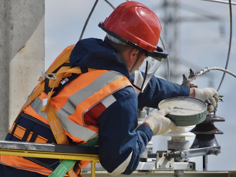 Engineer in a hi-vis jacket, harness and face shield working on overhead power line equipment